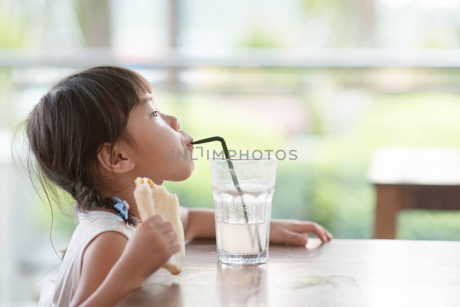 Little Asian child drinking and eating toast at cafe. Natural light outdoor lifestyle.