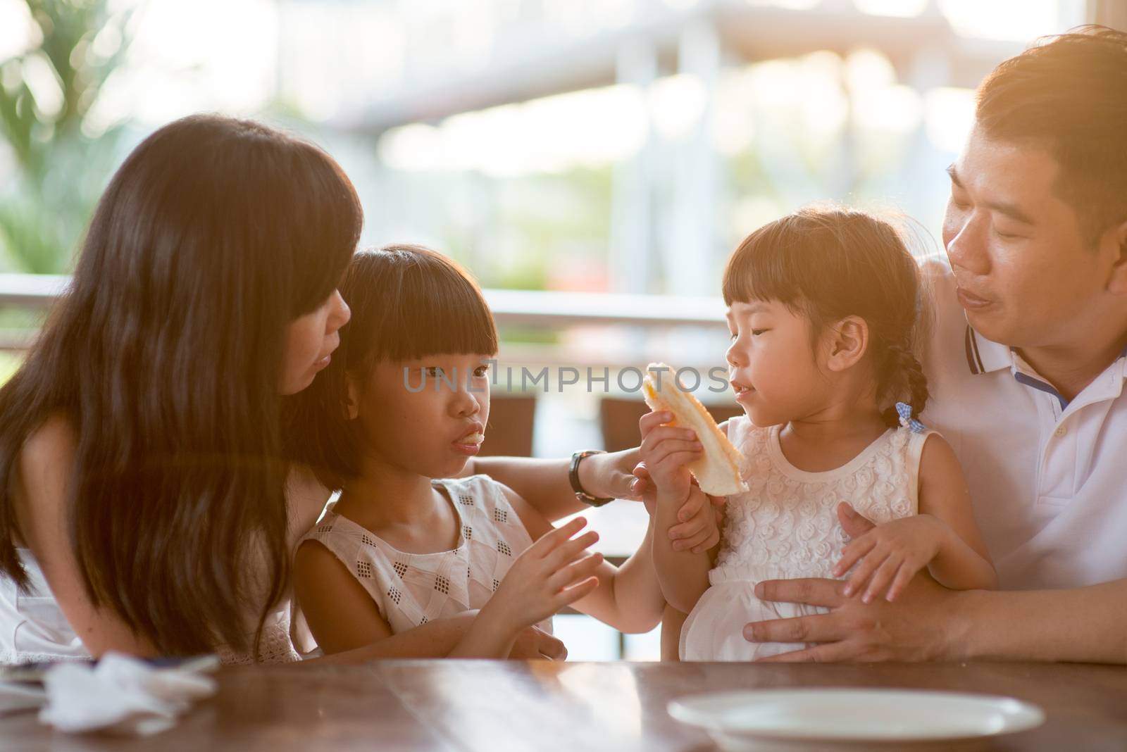 Happy children eating and sharing bread at cafeteria. Asian family outdoor lifestyle with natural light.