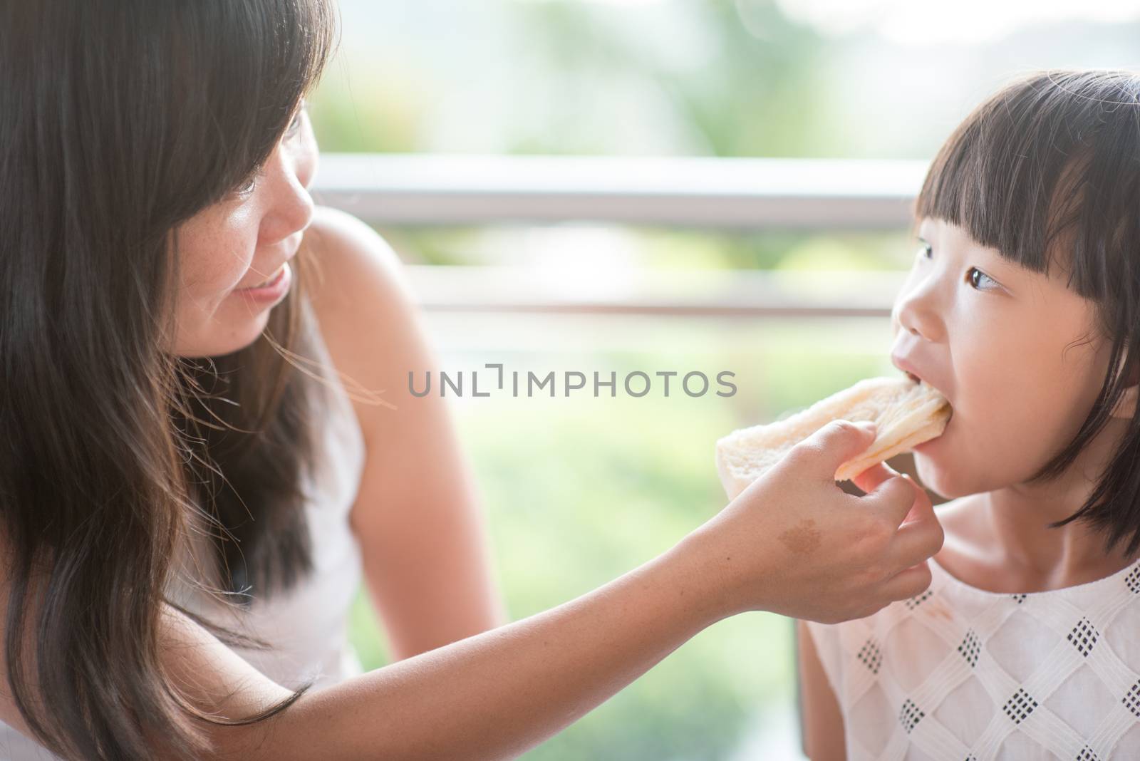 Mom feed bread to her child at cafe. Asian family outdoor lifestyle with natural light.