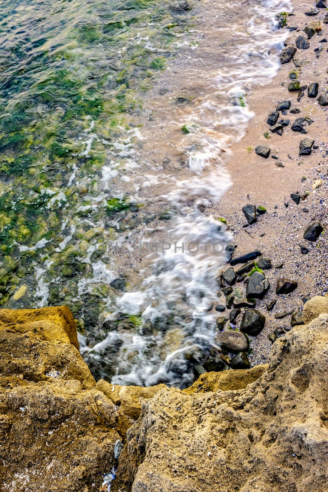 wave rolls onto the rocks of sandy coast by Pellinni