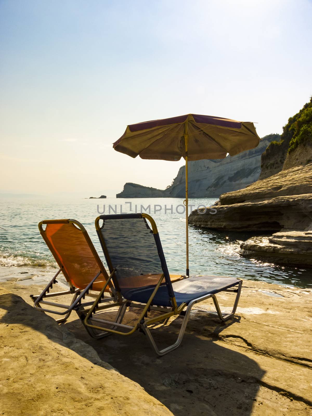 Sunbeds and umbrella on rocky beach in Corfu Island, Greece.