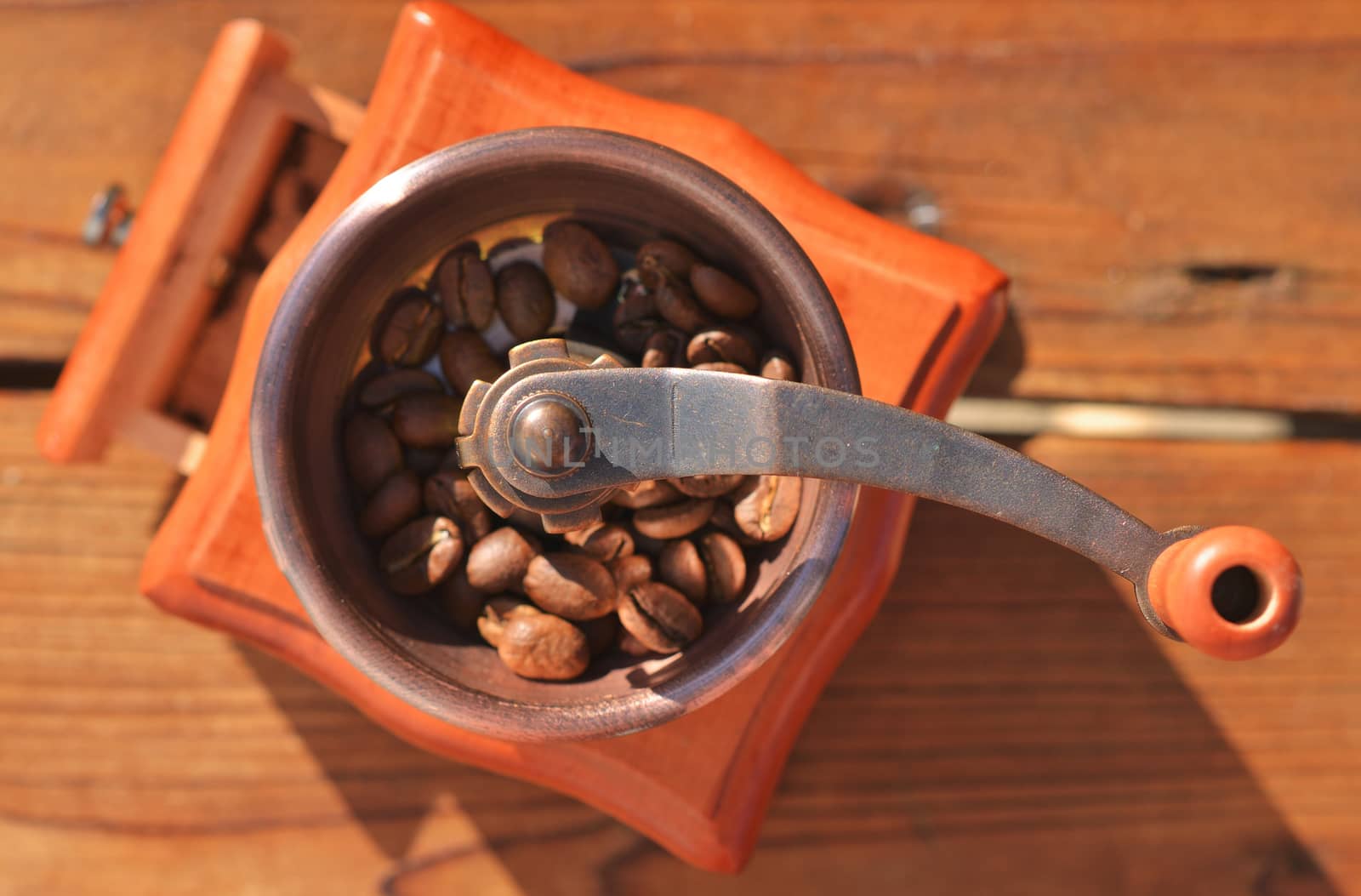 A handmade coffee grinder with large coffee beans on a wooden planks close-up