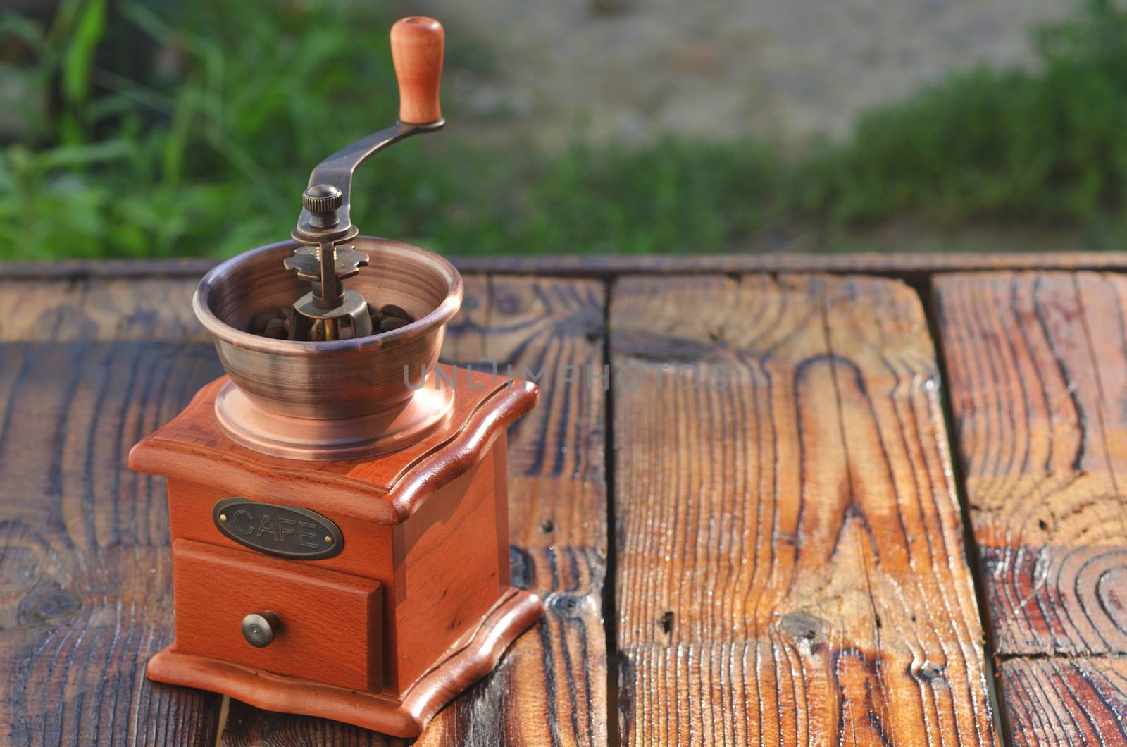 Manual horizontal coffee grinder with coffee beans on wooden boards against a background of green