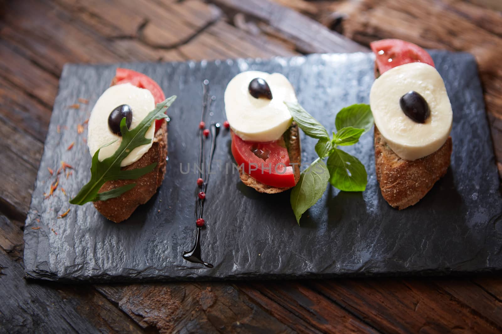Italian bruschetta with chopped tomatoes, basil, mozzarella cheese and balsamic vinegar. Fresh homemade caprese bruschetta or crostini over black stone background, copy space.