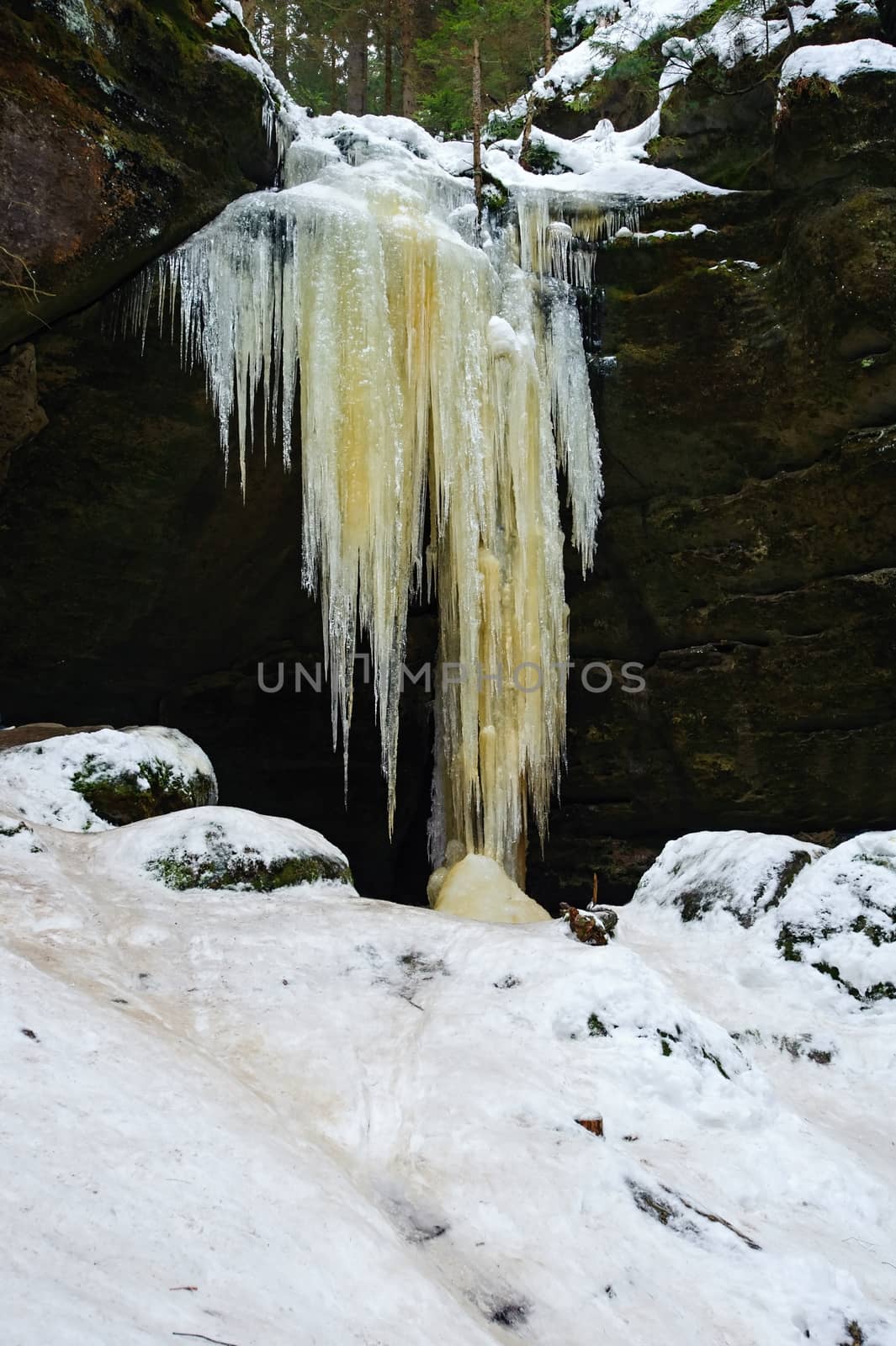 Frozen waterfalls on the rock, orange colored and snow