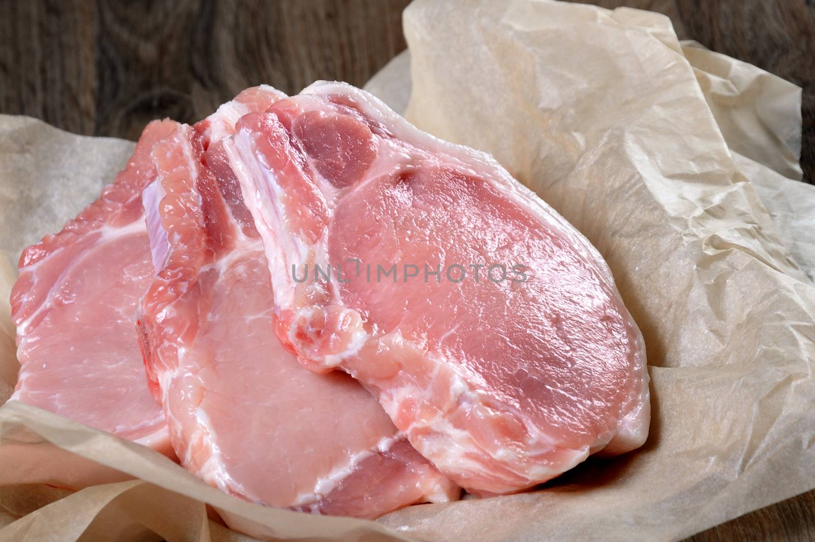A pile of fresh chopped raw pork steaks over the bones in the wrapping paper on the table. Close-up.