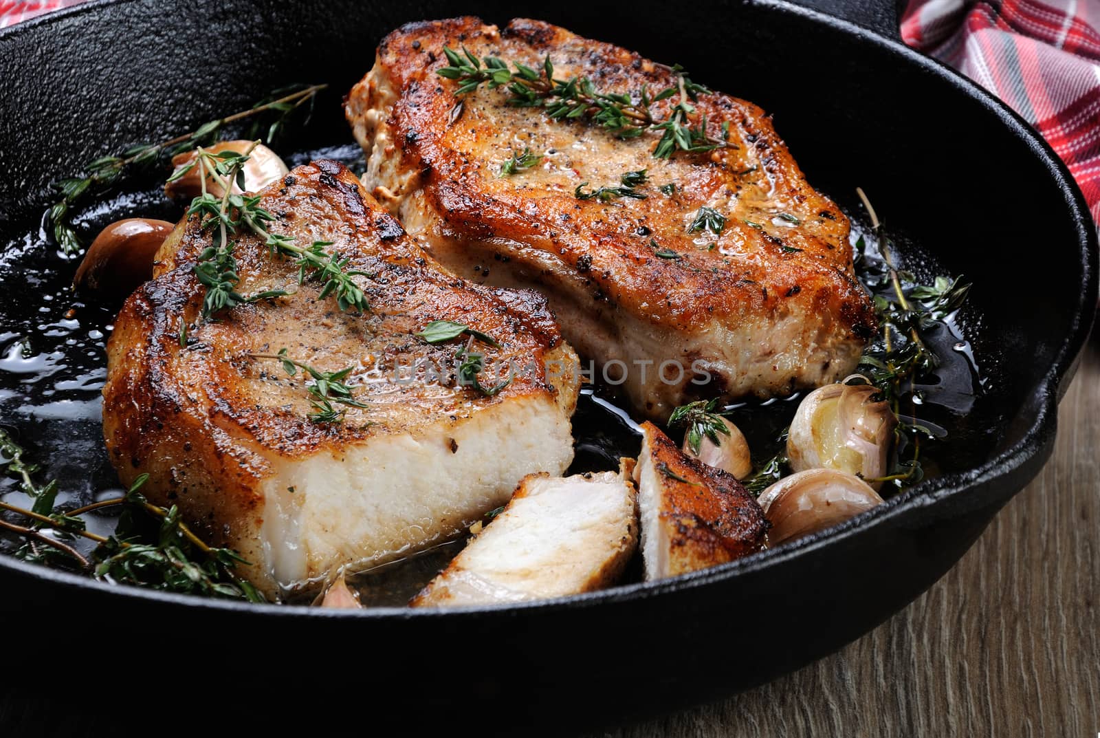 Fried pork steak in oil with herbs and garlic  in a cut in the frying pan. Close-up.