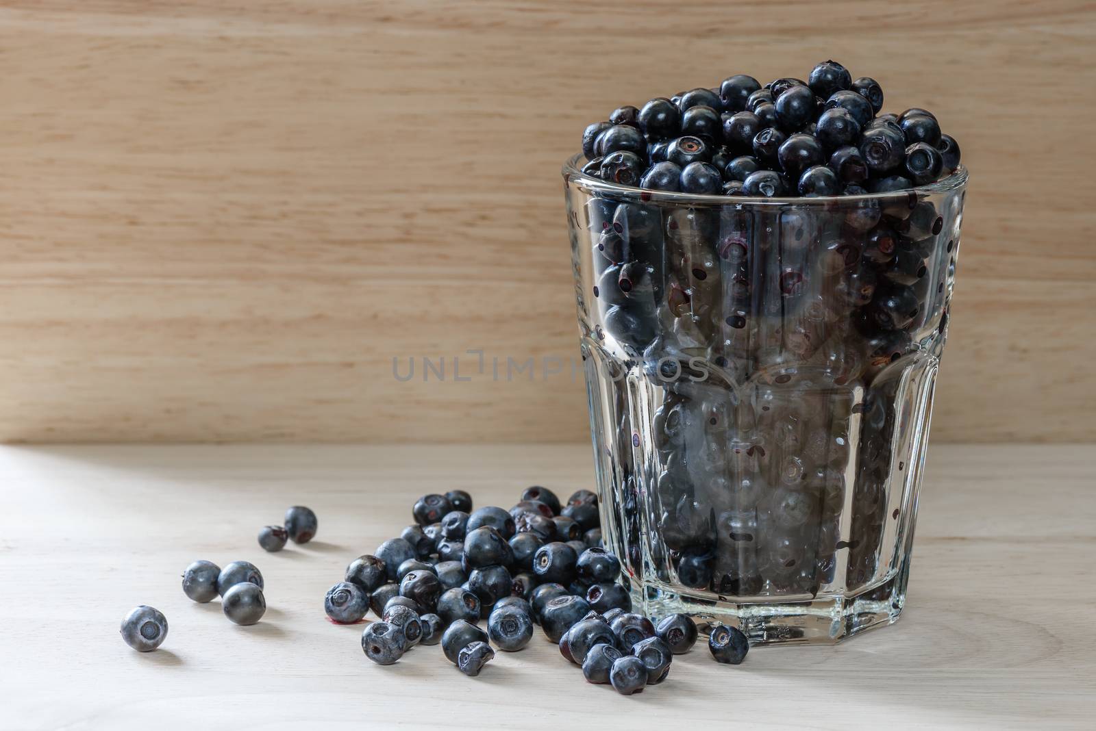 Blueberries in a glass with scattered berries. Good addition for breakfast