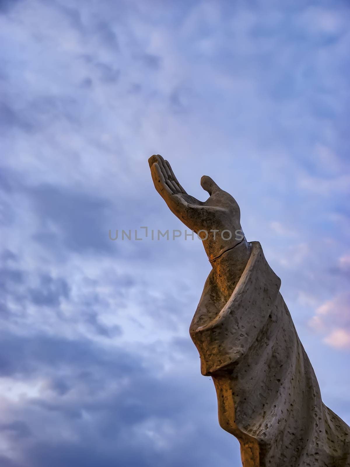Hand of Jesus statue on the road on the island Corfu, Greece. In the background the sky with clouds.