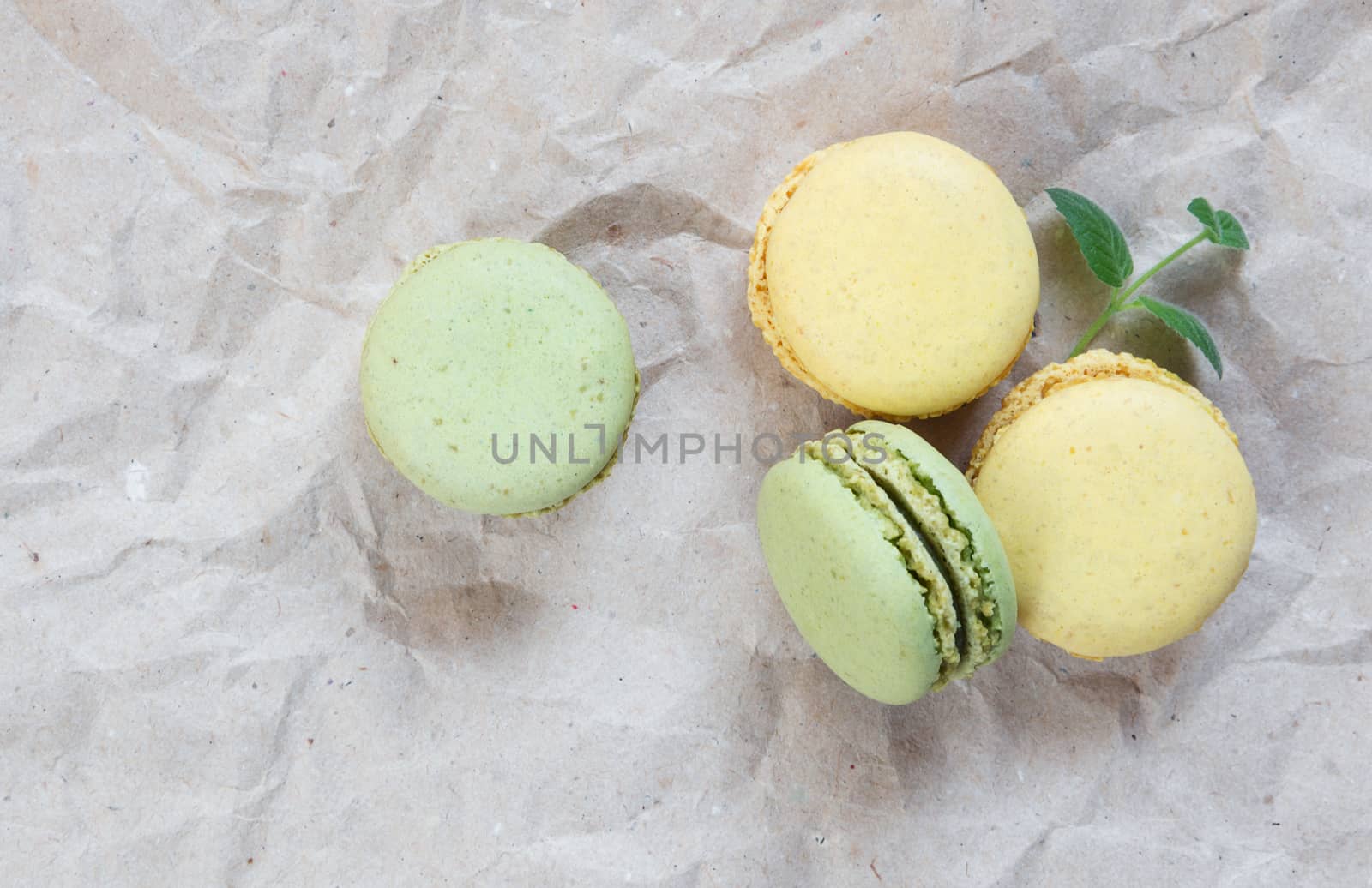 Green and yellow almond cookies (macaroons) and green mint leaves on the background of crumpled craft paper; top view, flat lay composition