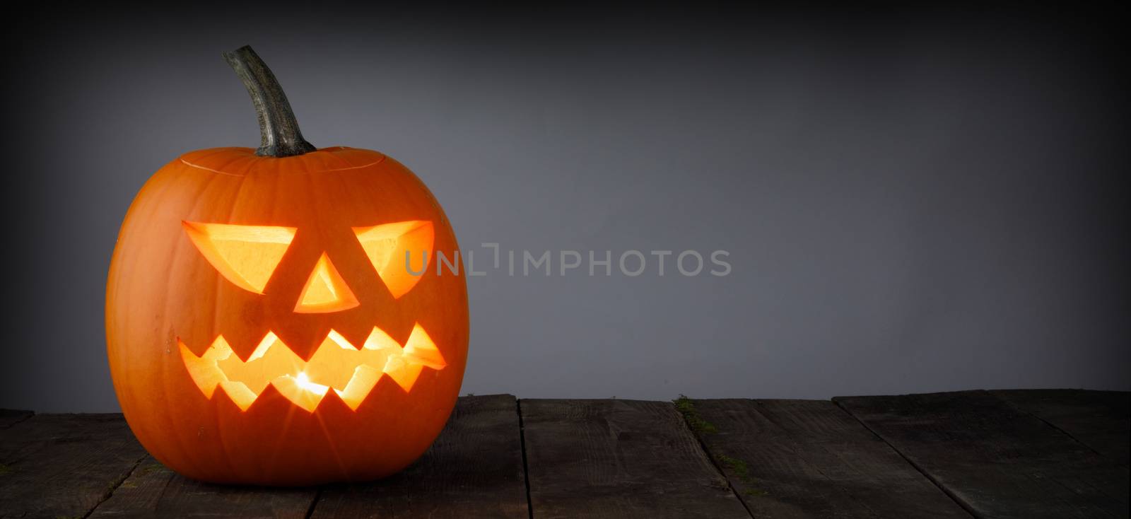 Glowing Halloween pumpkin head jack lantern on gray old wooden background