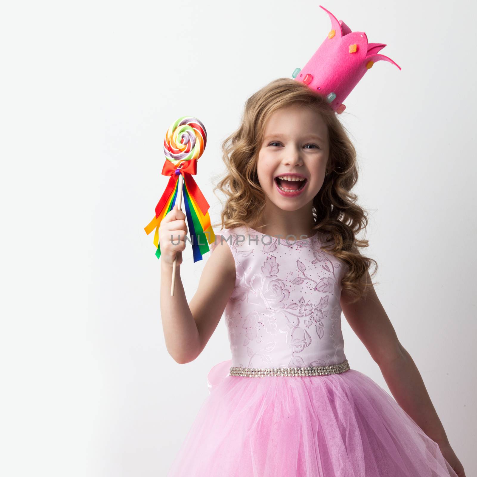 Beautiful little candy princess girl in crown holding big lollipop and smiling