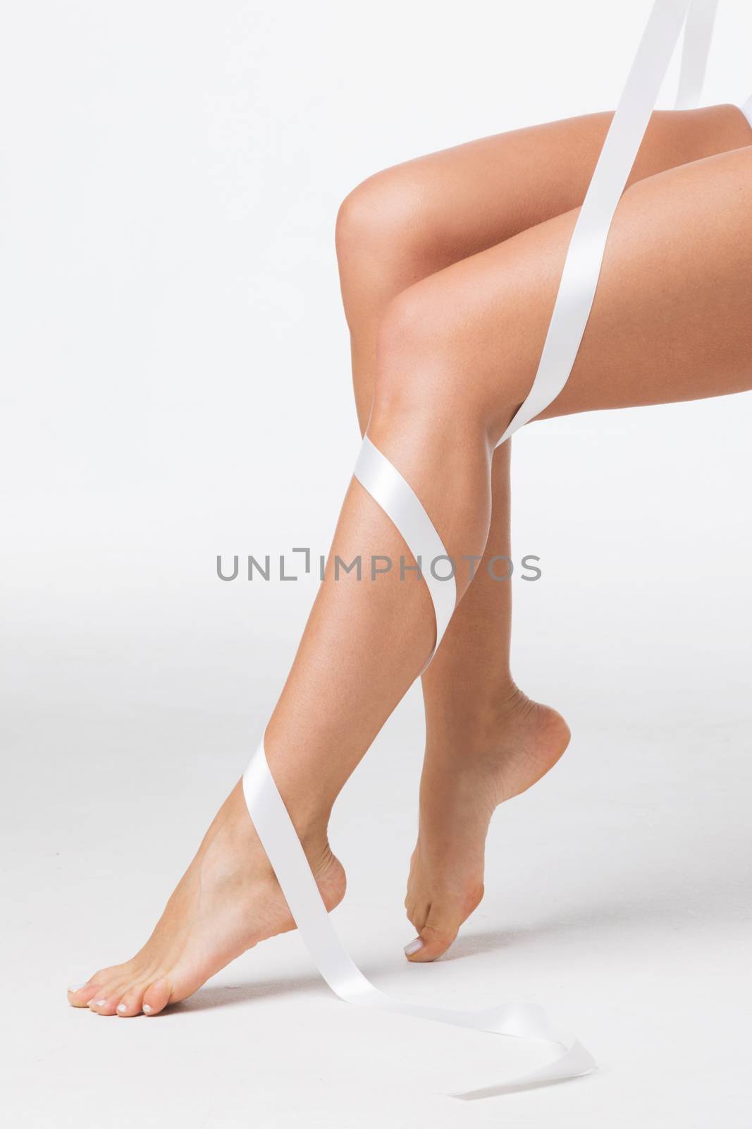 Closeup of perfect women's legs with white ribbon on white background