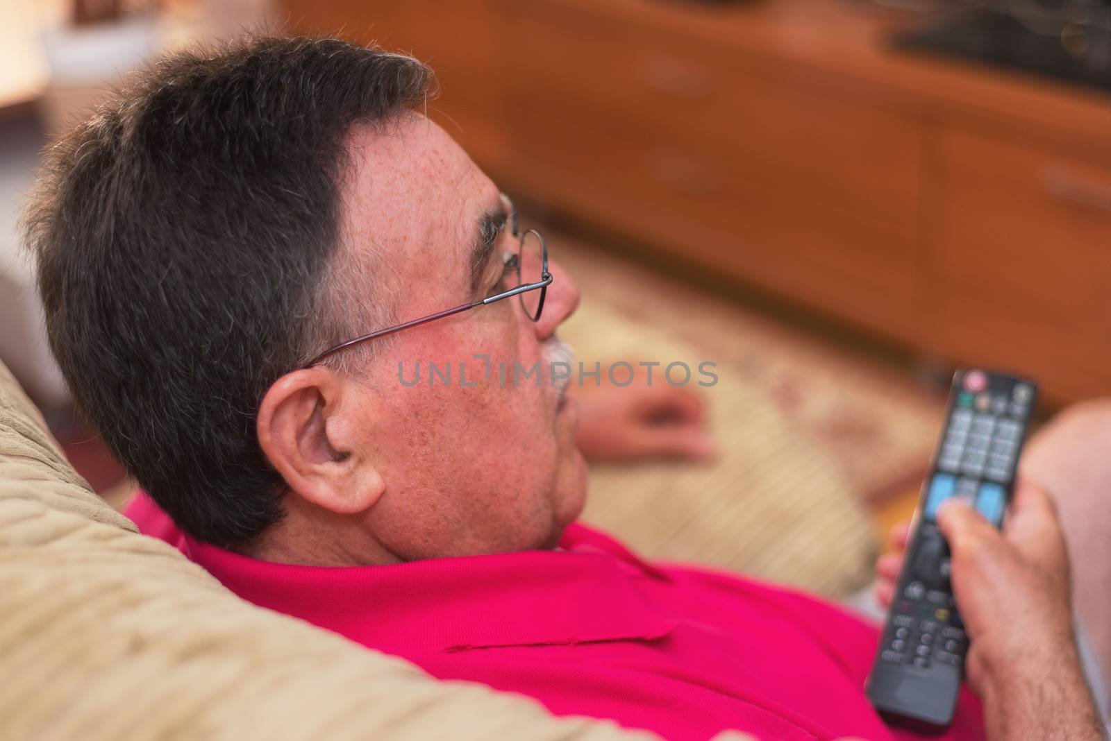 Back view of senior man watching tv holding remote control