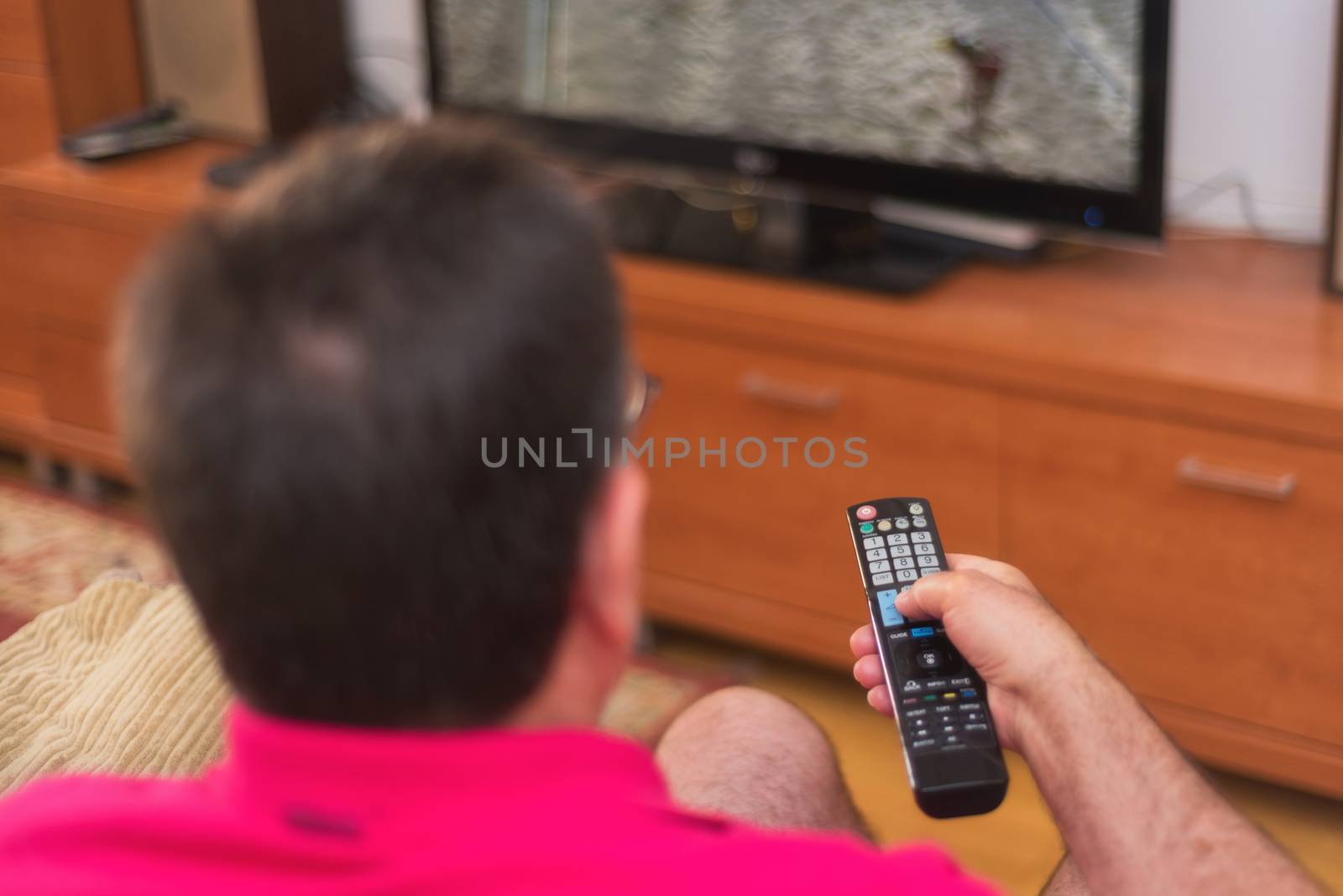 Back view of senior man watching tv holding remote control by HERRAEZ