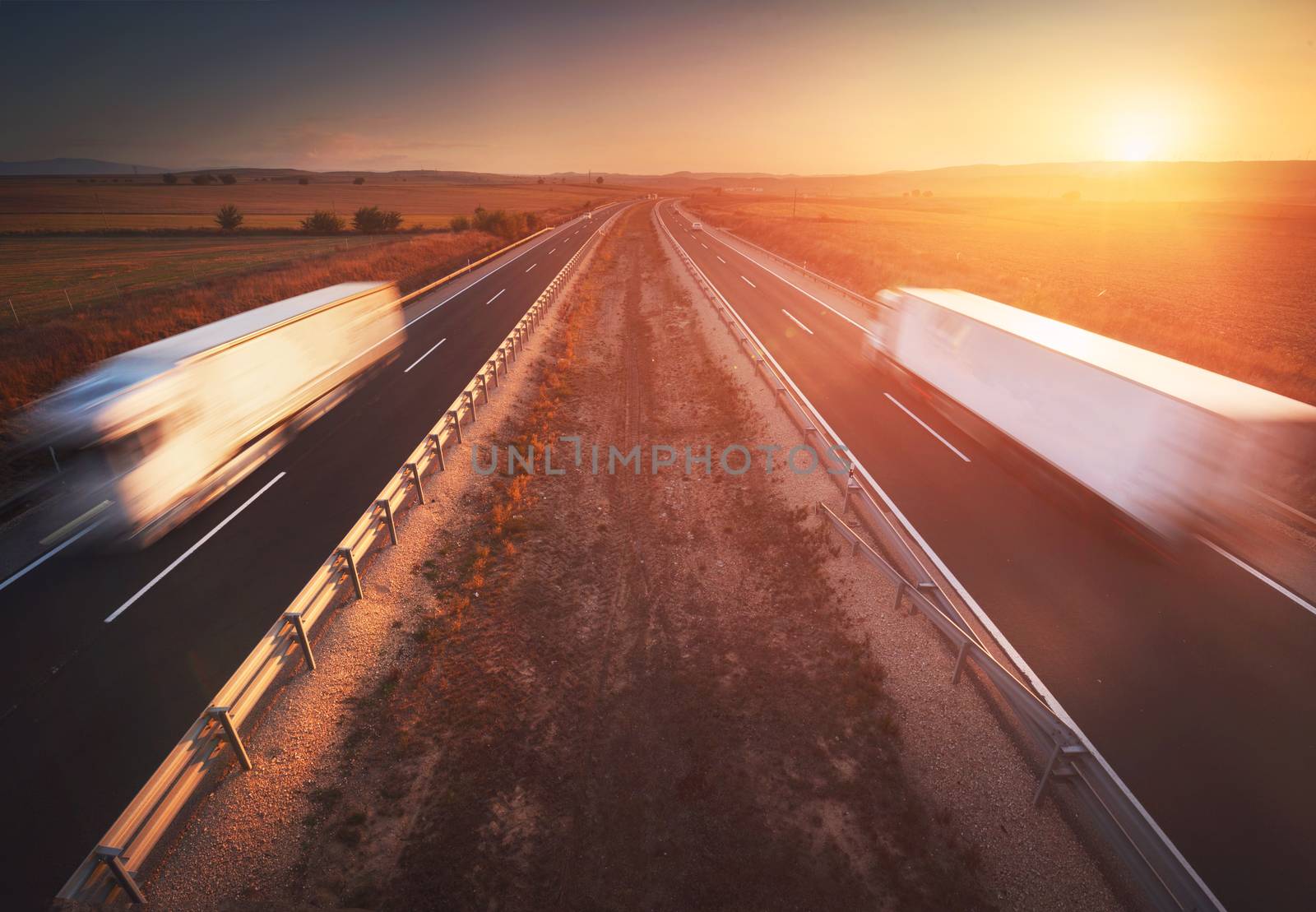 Trucks in the highway, dramatic sunset, motion blur. Cargo, transportation concept by HERRAEZ