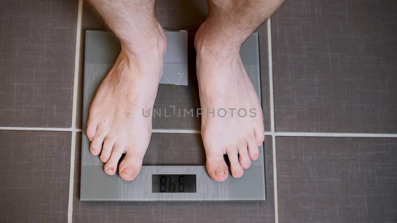 Male feet on glass scales, men's diet, body weight, close up, man standing on scales, top down view