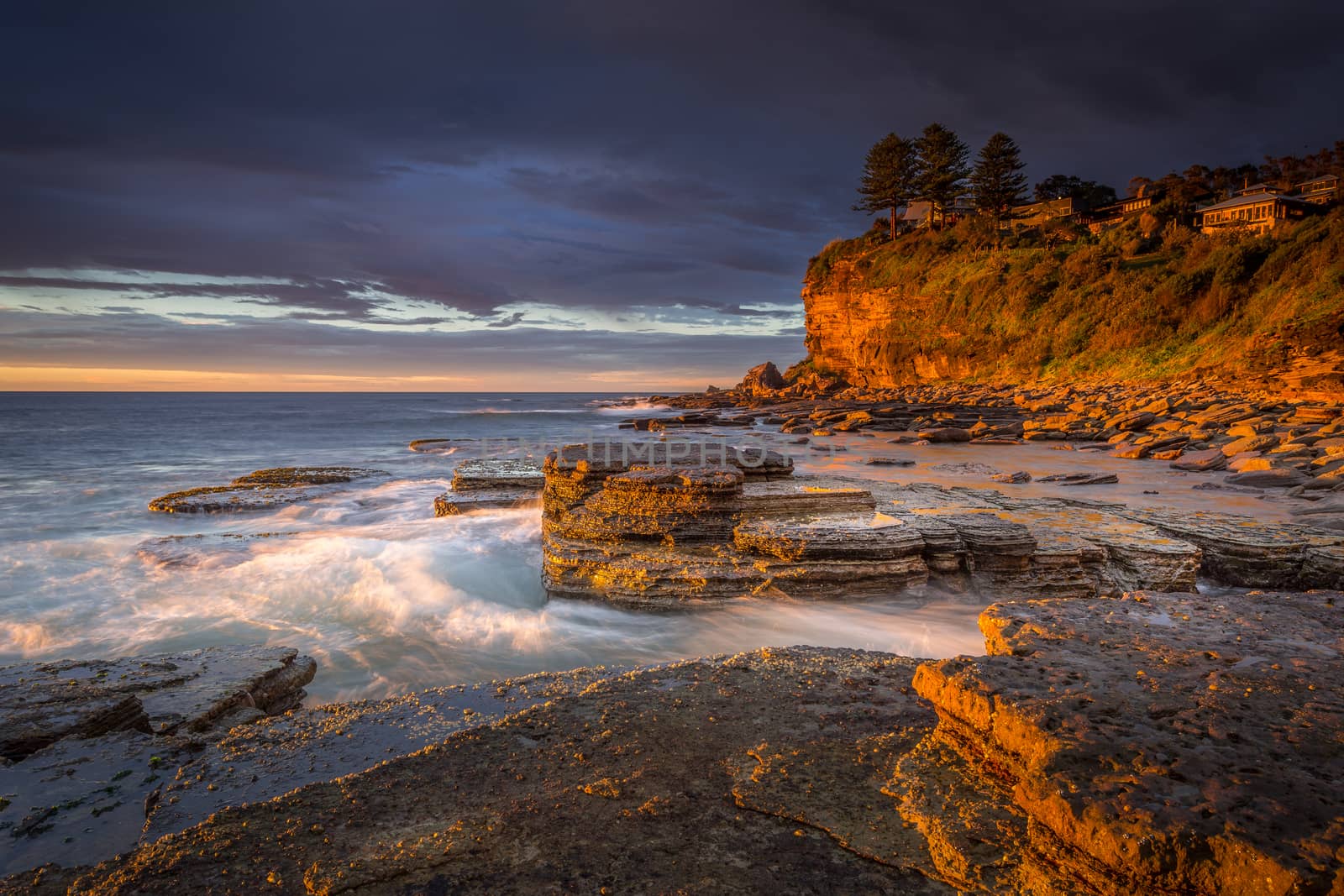 First light at Avalon beach, rich golden orange tones of light striking the cliff faces and rocks