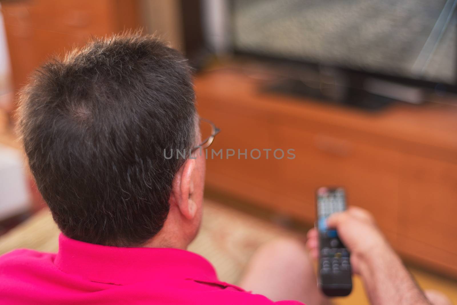 Back view of senior man watching tv holding remote control