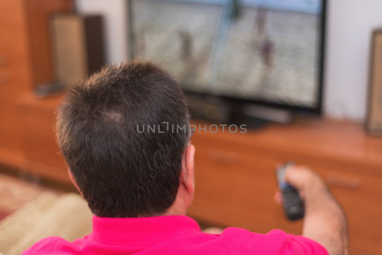 Back view of senior man watching tv holding remote control by HERRAEZ