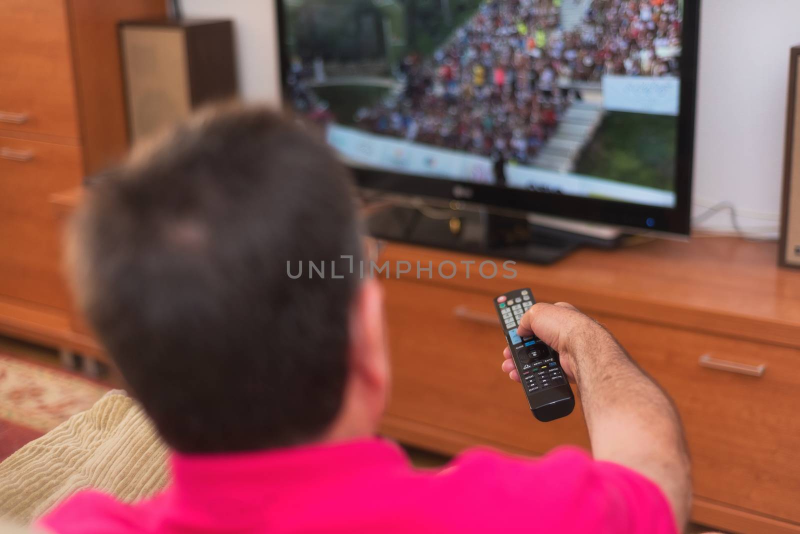 Back view of senior man watching tv holding remote control by HERRAEZ