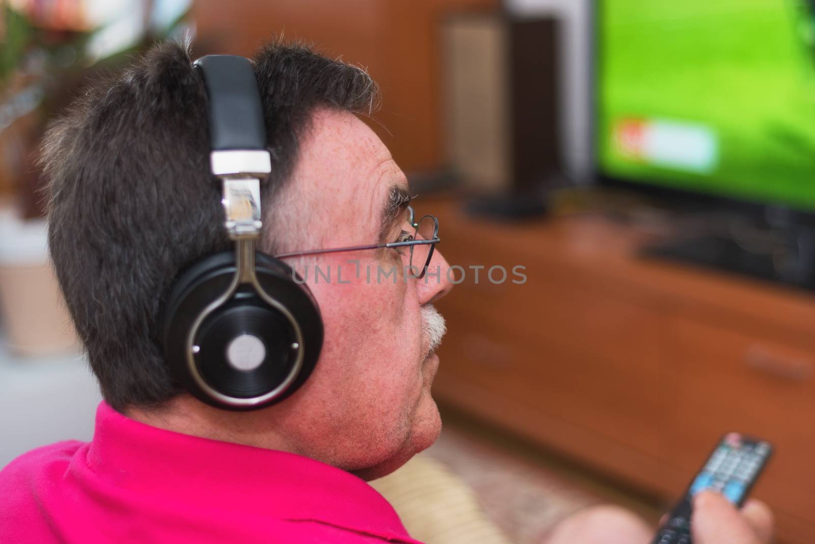 Back view of senior man watching tv holding remote control by HERRAEZ