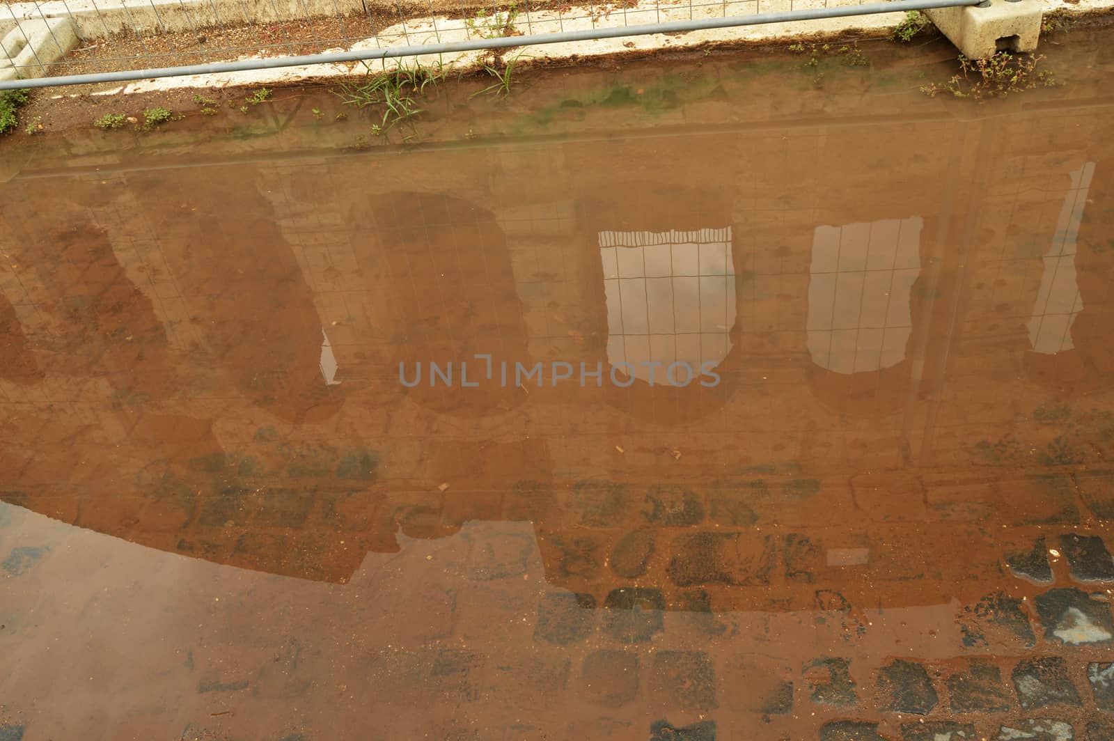 The Colosseum is reflected in a puddle with a brown background, unusual foreshortening sights of Rome Italy.