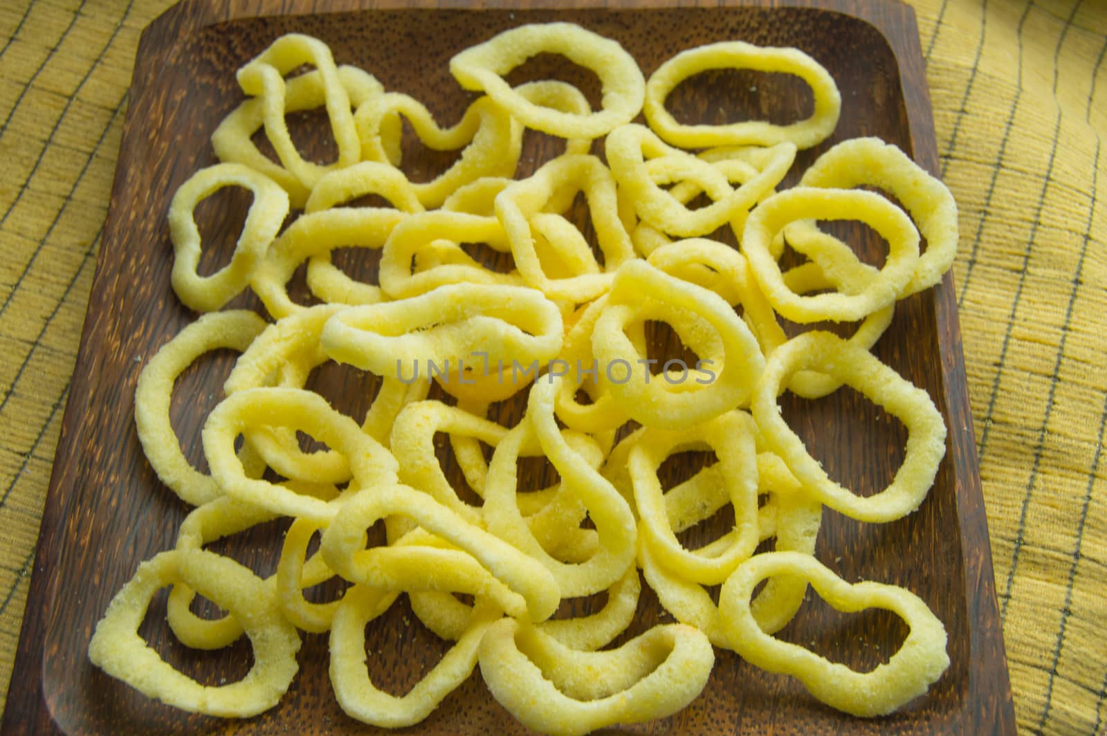 Delicious crispy rings of onion chips lie on a dark wooden plate on a yellow napkin background.