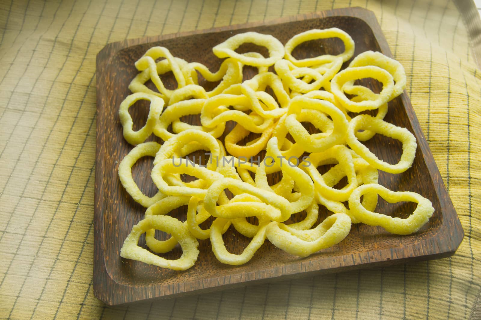 Delicious crispy rings of onion chips lie on a dark wooden plate on a yellow napkin background.