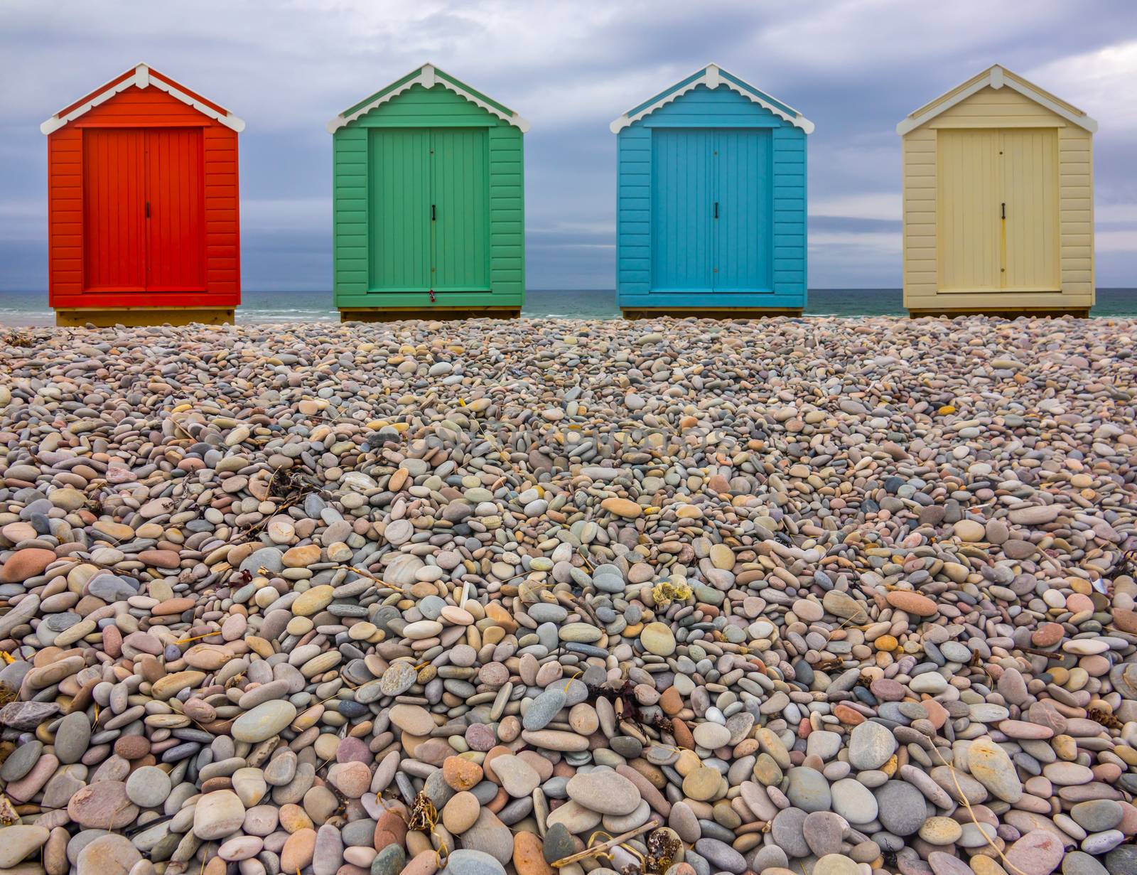 Vintage British Beach Huts On A Stony Shore With Wintry Sky With Copy Space (Focus On Foreground)