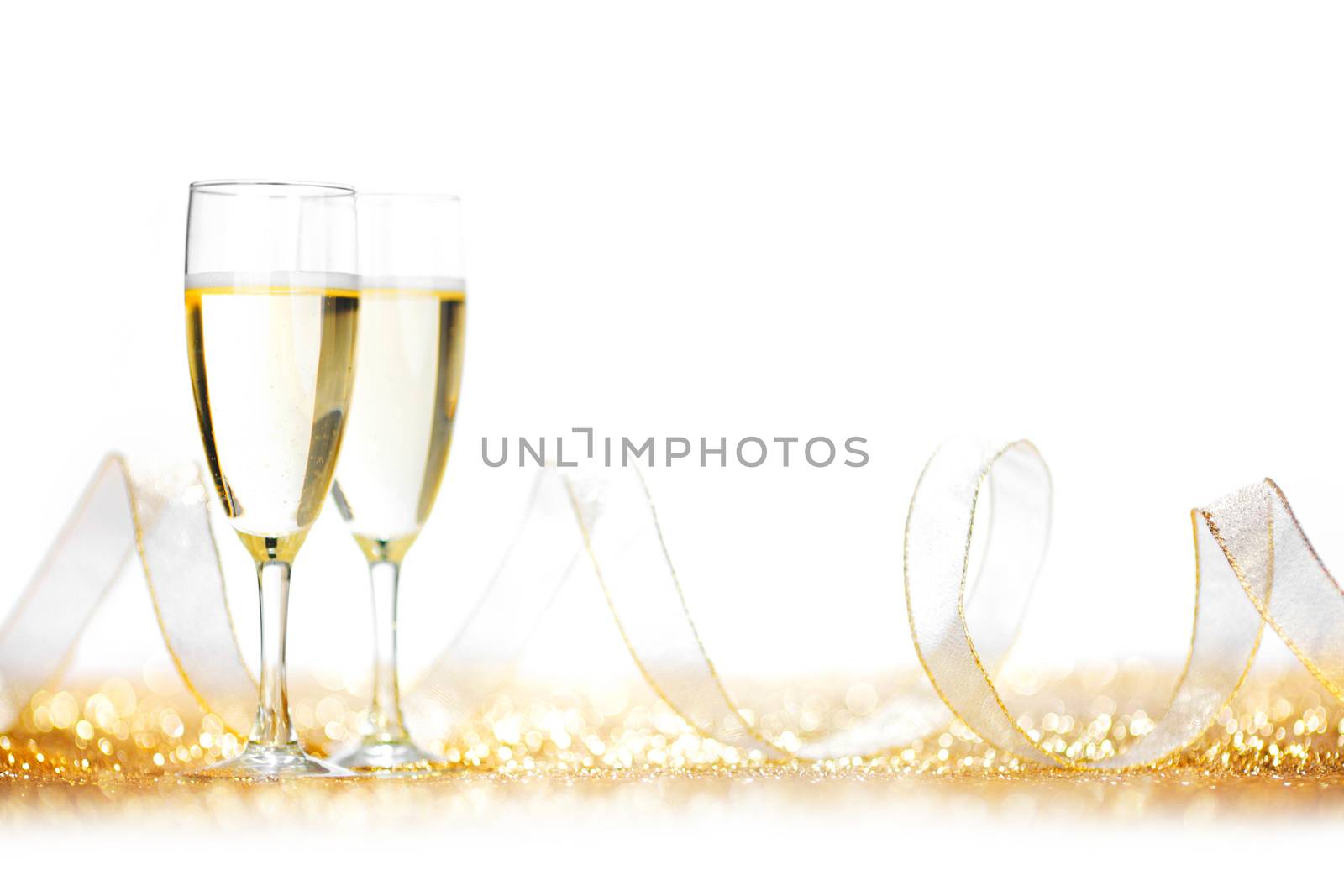 Glasses of champagne and ribbon on golden glitters isolated on white