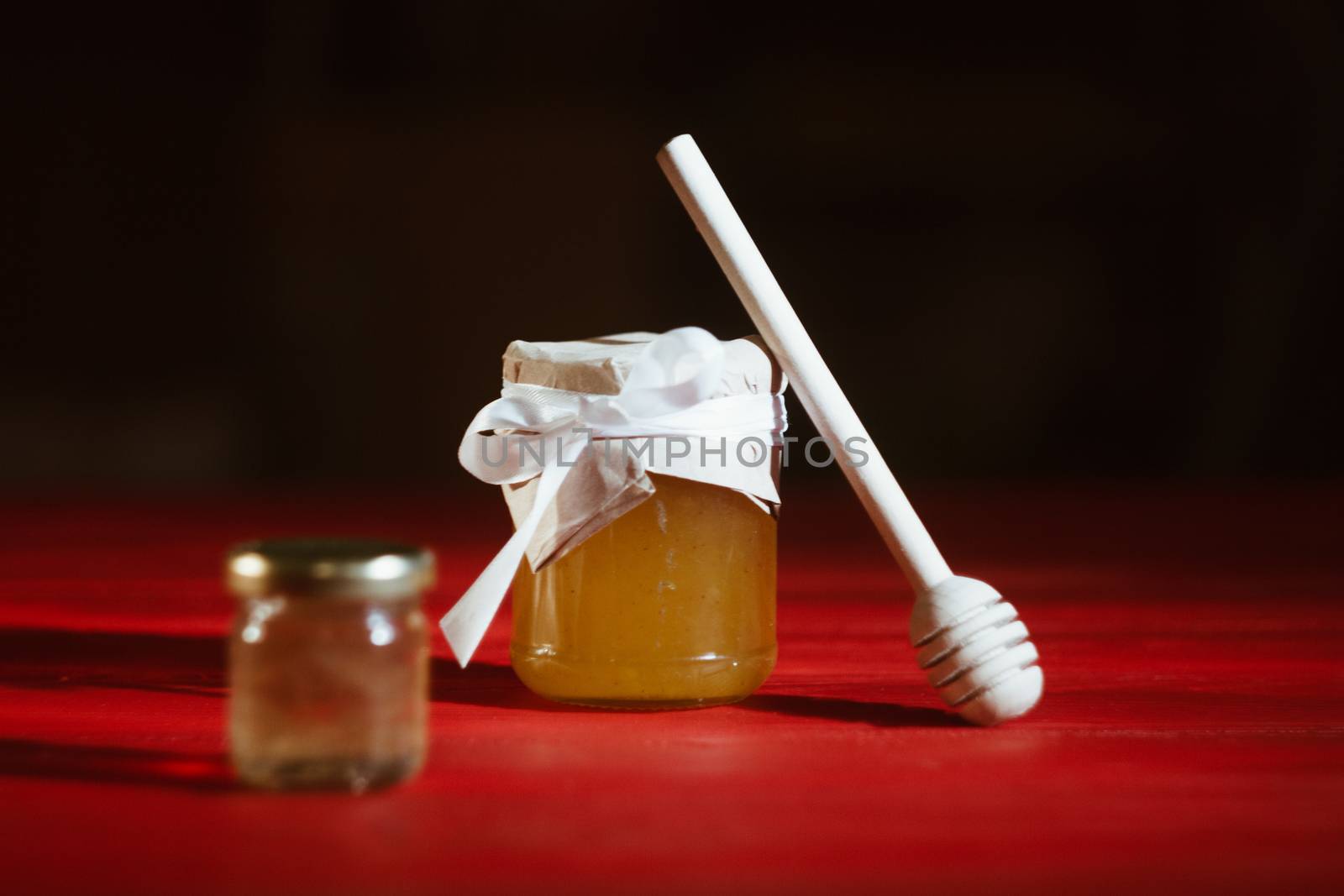 Honey in a glass jar close up on a black background on a red wooden table. pour honey with a stick honey dipper by yulaphotographer
