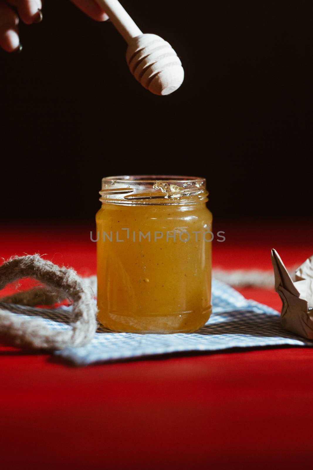 Honey in a glass jar close up on a black background on a red wooden table. pour honey with a stick honey dipper by yulaphotographer