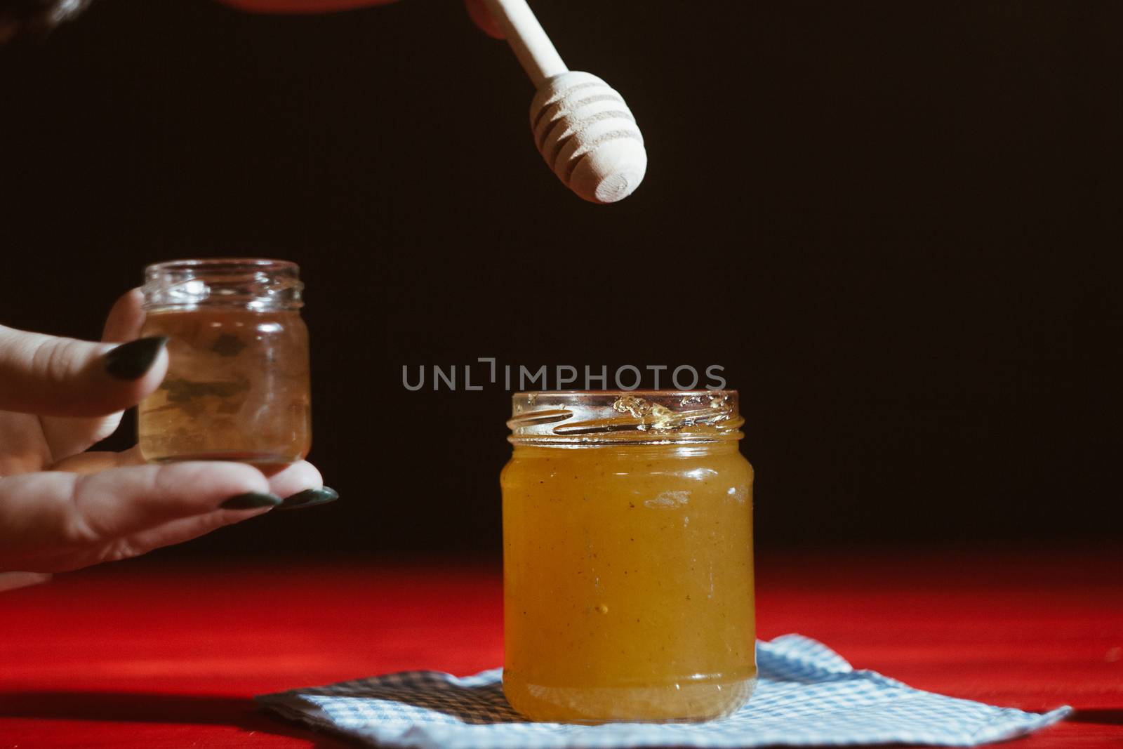 Hand with dipper picking honey from a jar of honey. Jars of honey, bee honeycomb and bee pollen on wooden table