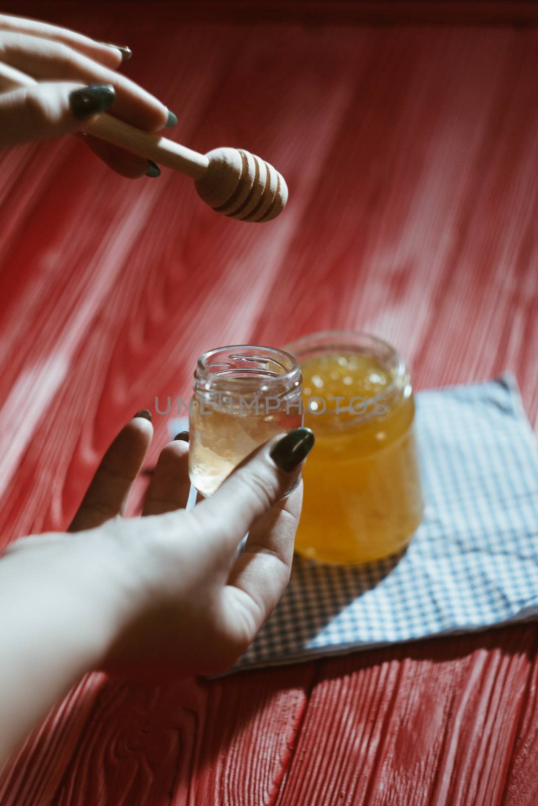 Hand with dipper picking honey from a jar of honey. Jars of honey, bee honeycomb and bee pollen on wooden table