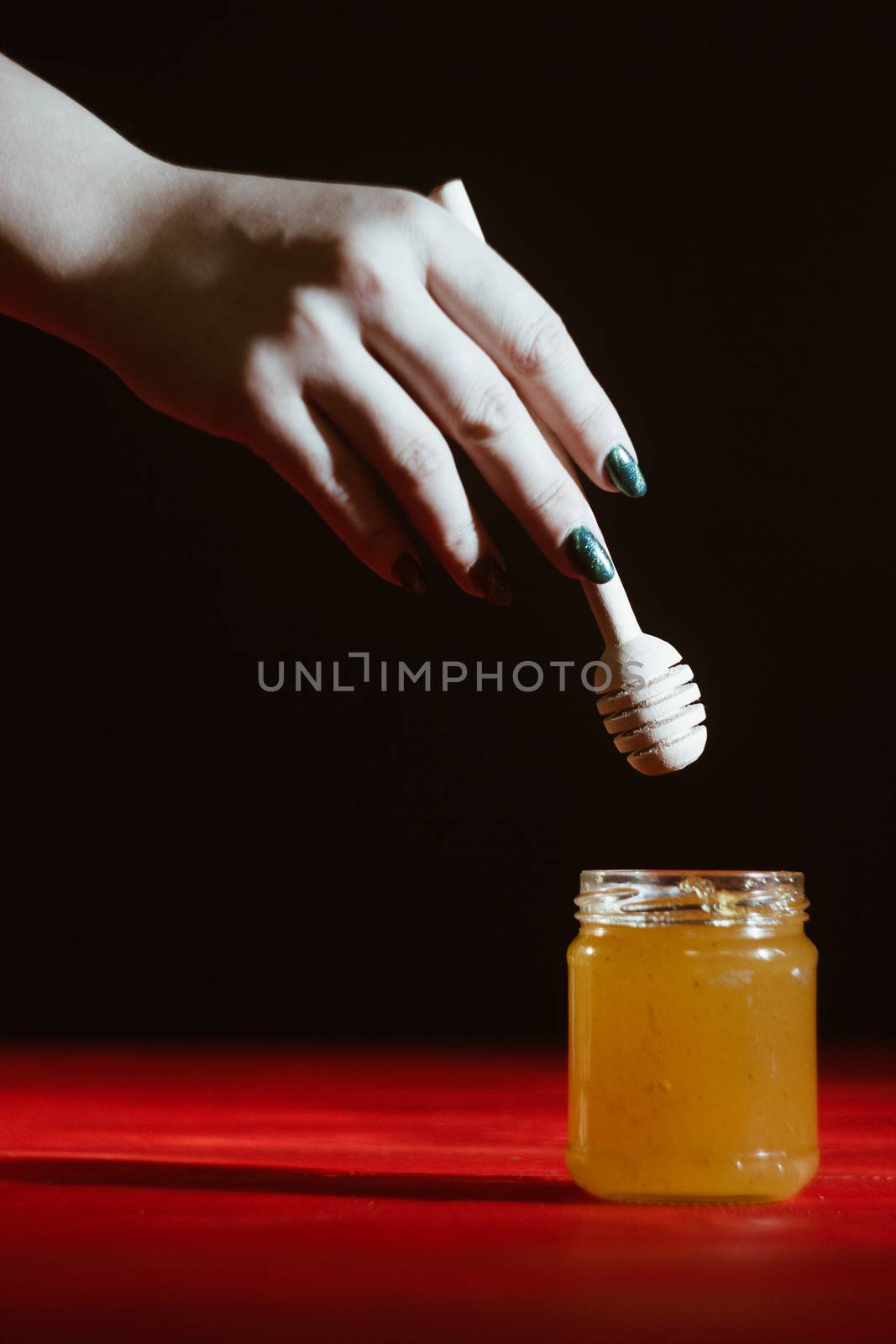 Hand with dipper picking honey from a jar of honey. Jars of honey, bee honeycomb and bee pollen on wooden table