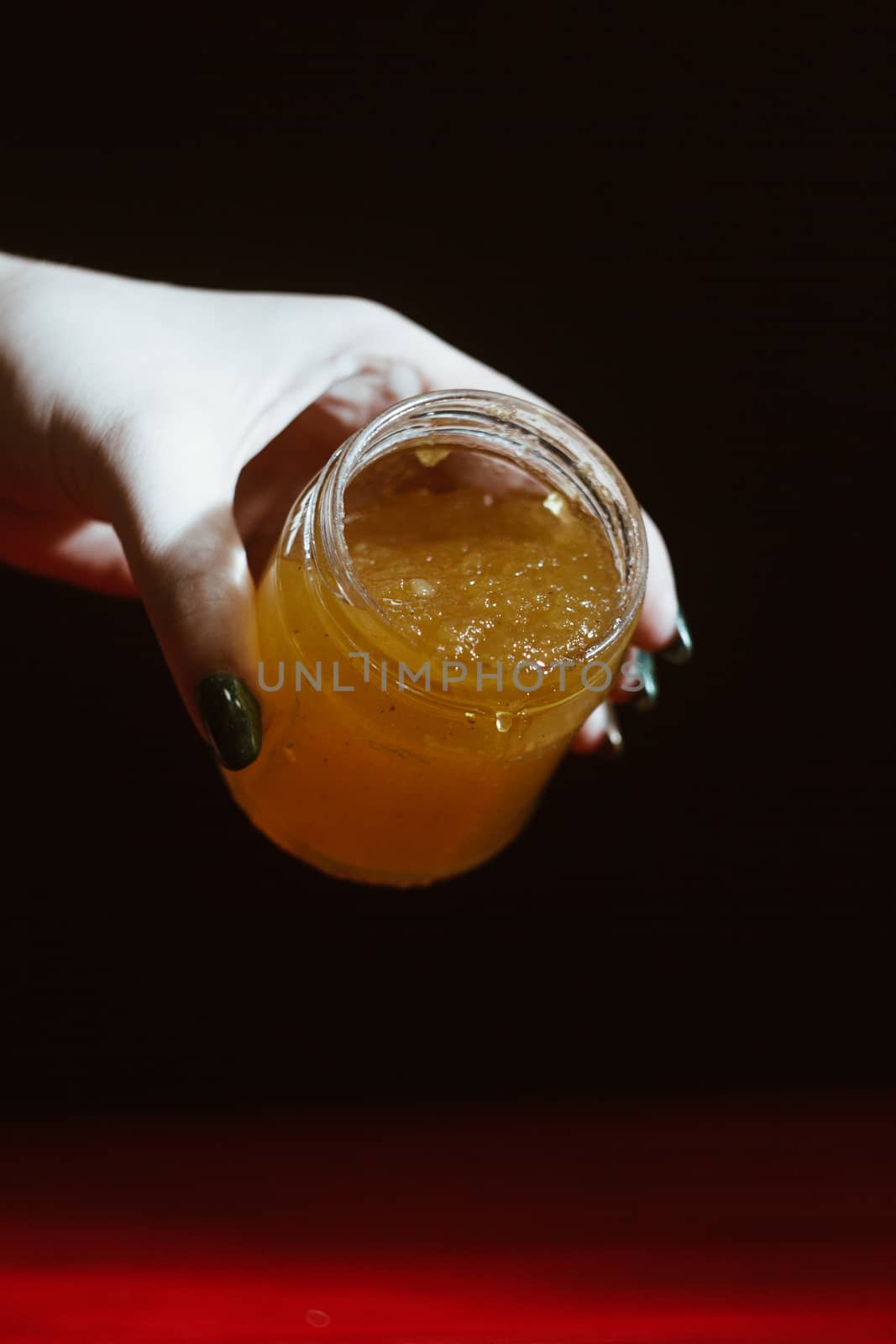 Hand with dipper picking honey from a jar of honey. Jars of honey, bee honeycomb and bee pollen on wooden table