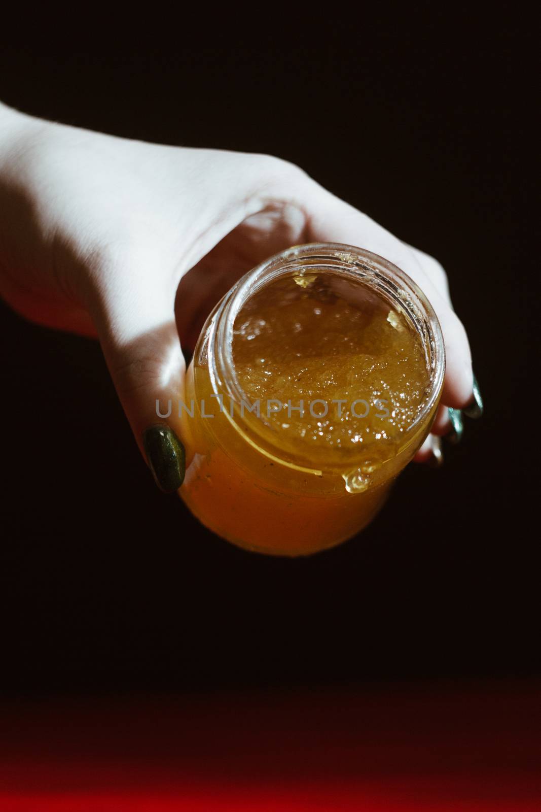 Hand with dipper picking honey from a jar of honey. Jars of honey, bee honeycomb and bee pollen on wooden table