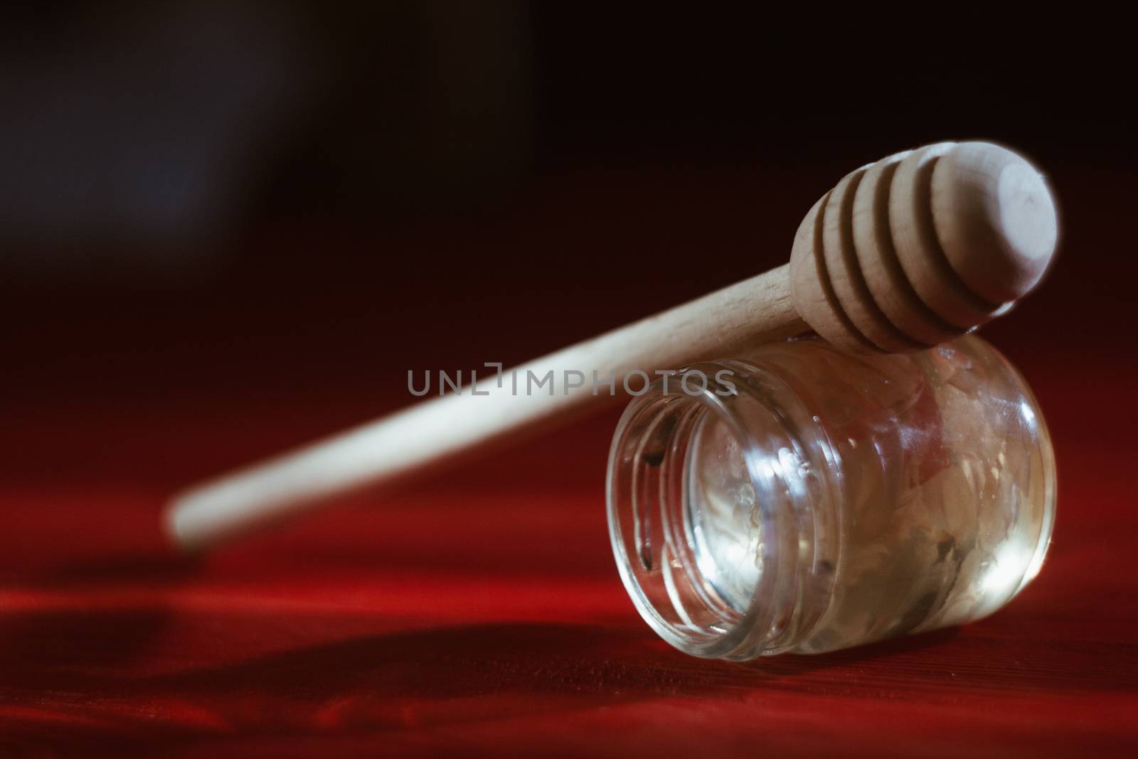 Honey in a glass jar close up on a black background on a red wooden table. pour honey with a stick honey dipper by yulaphotographer