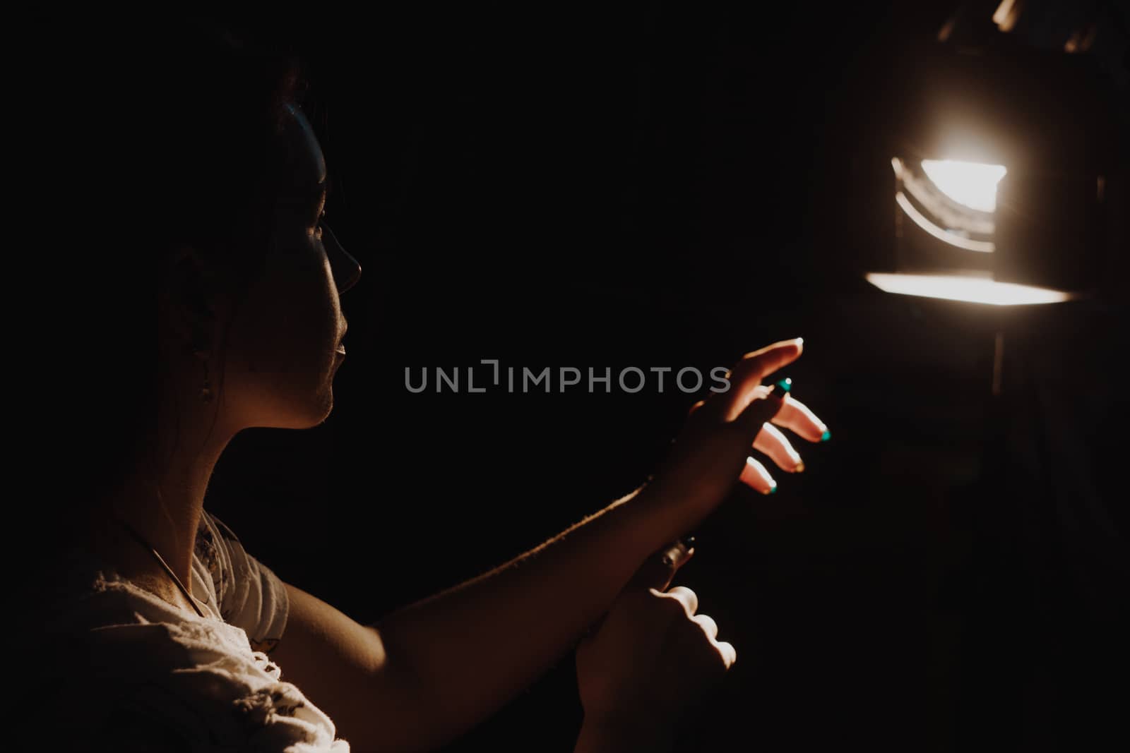 girl reaching for the light of the lantern, wooman in a dark room. illuminated hands with spotlight