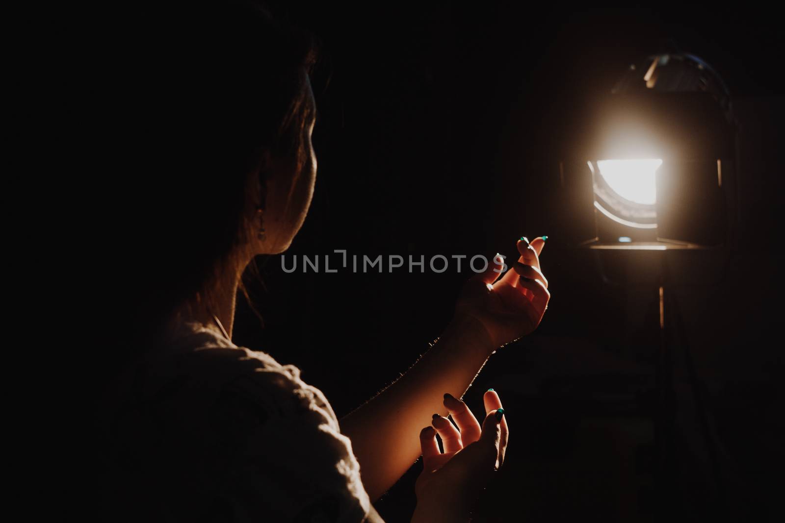 girl reaching for the light of the lantern, wooman in a dark room. illuminated hands with spotlight
