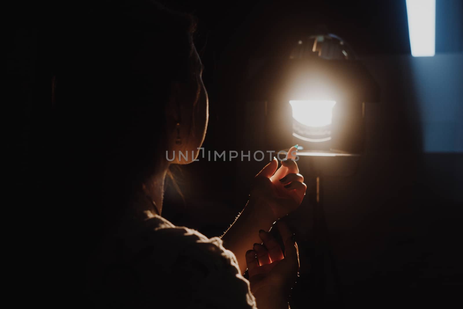 girl reaching for the light of the lantern, wooman in a dark room. illuminated hands with spotlight