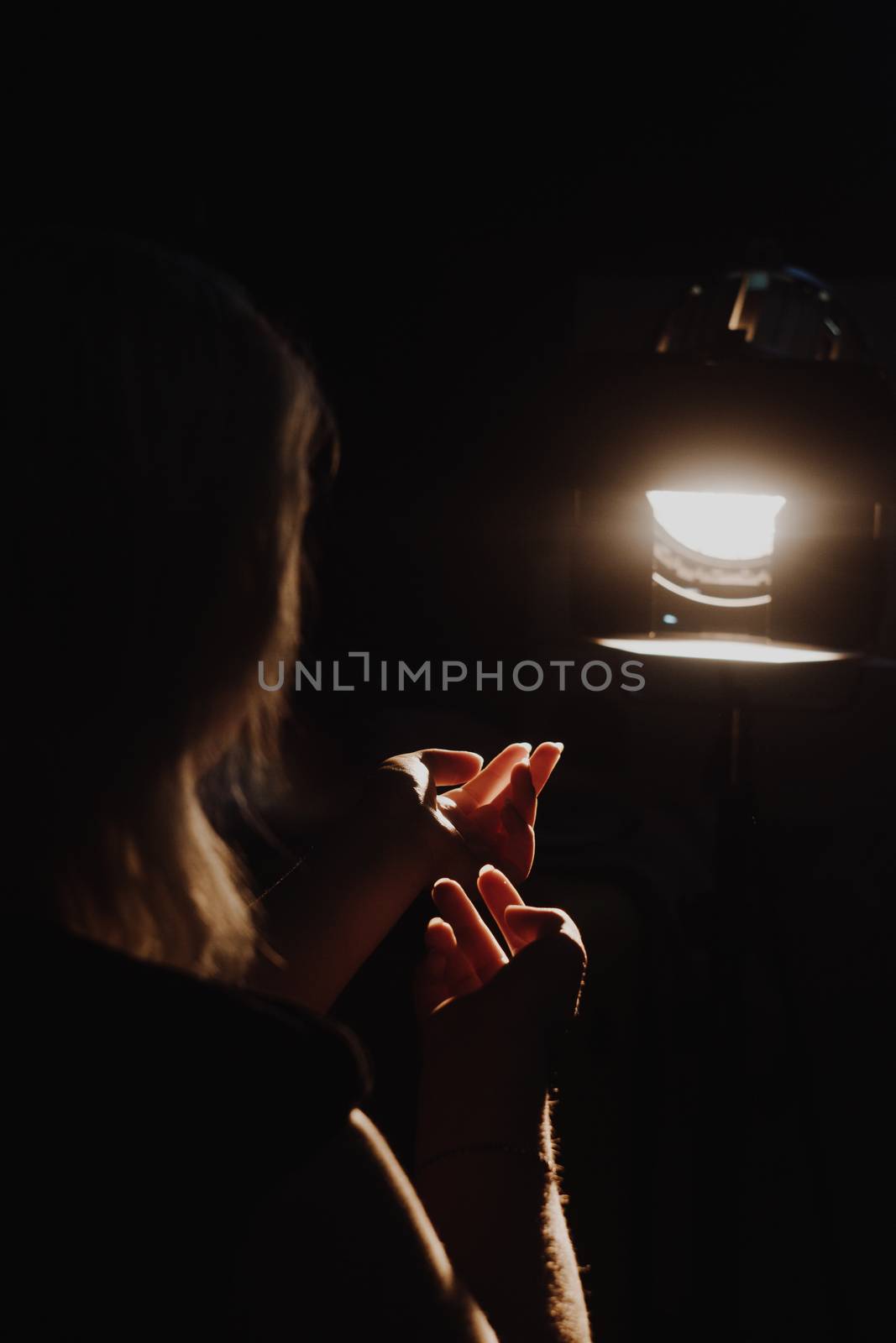 girl reaching for the light of the lantern, wooman in a dark room. illuminated hands with spotlight