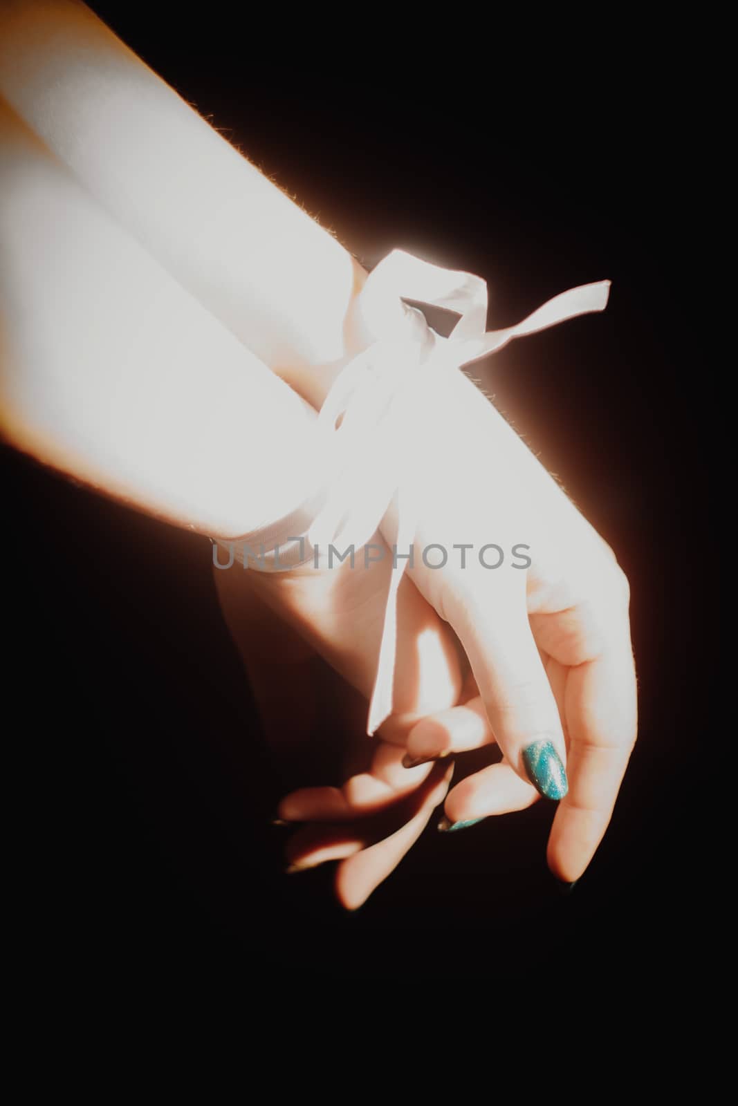 tied hands with white ribbon isolated on black background highlighted with light by yulaphotographer