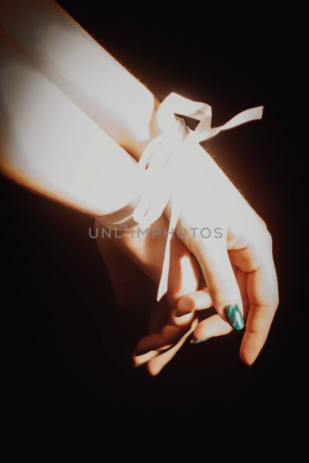 tied hands with white ribbon isolated on black background highlighted with light by yulaphotographer