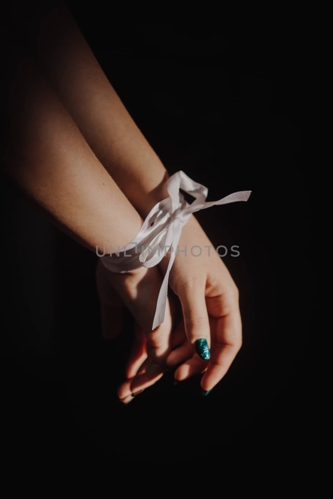 tied hands with white ribbon isolated on black background highlighted with light by yulaphotographer