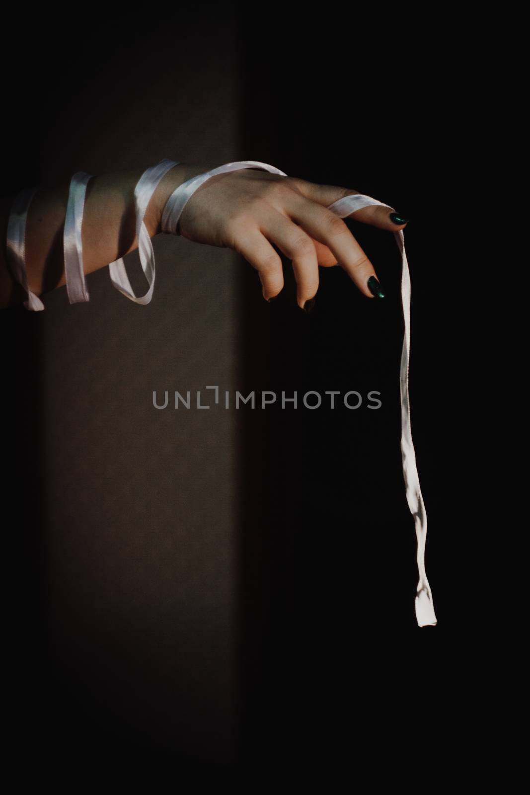 tied hands with white ribbon isolated on black background highlighted with light by yulaphotographer