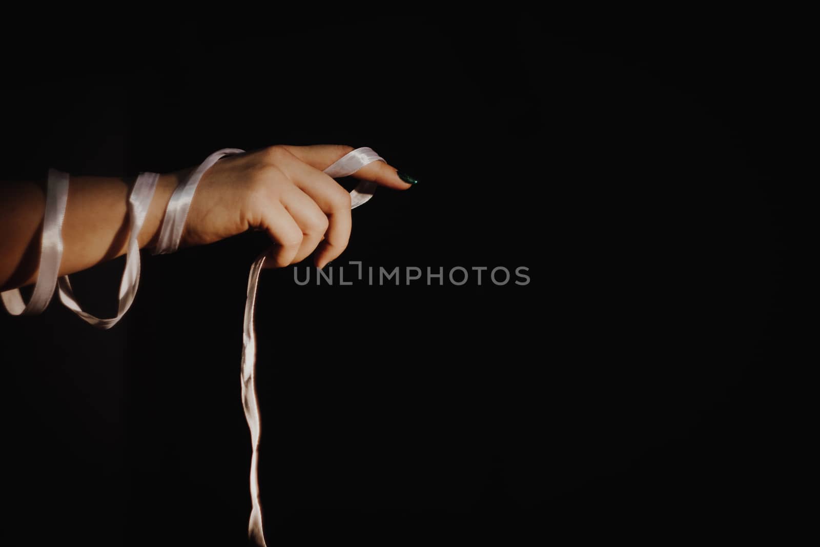 tied hands with white ribbon isolated on black background highlighted with light by yulaphotographer