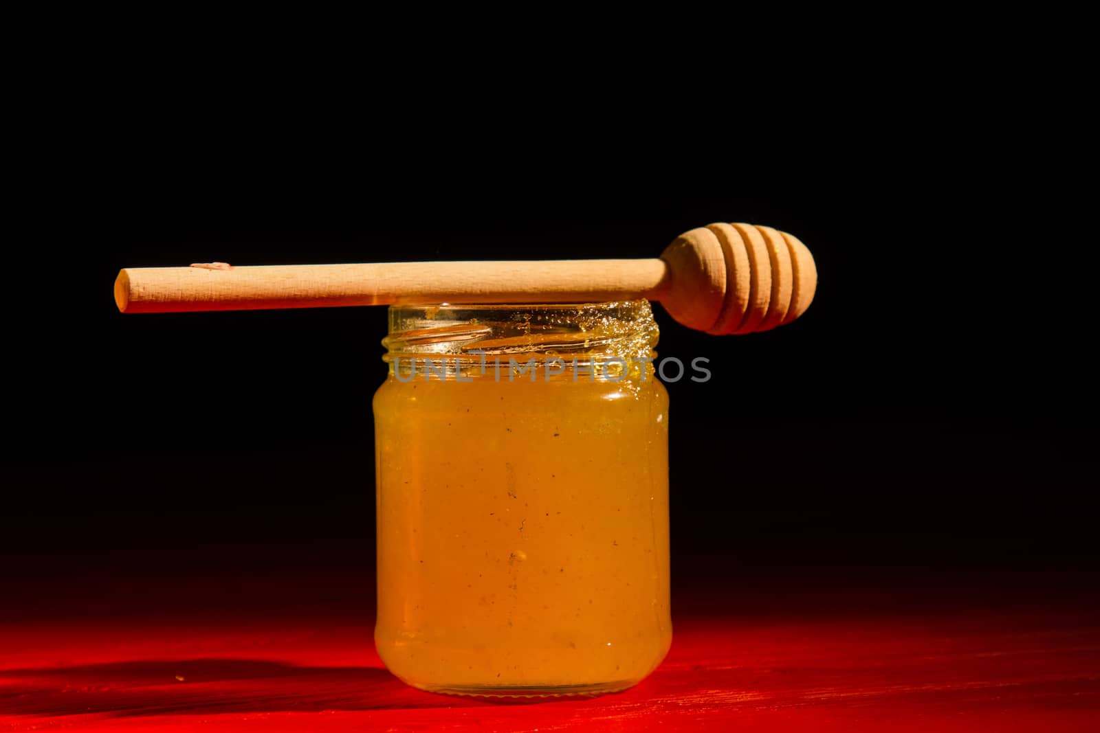 Honey with dipper on red wooden background with the the play of light and shadow