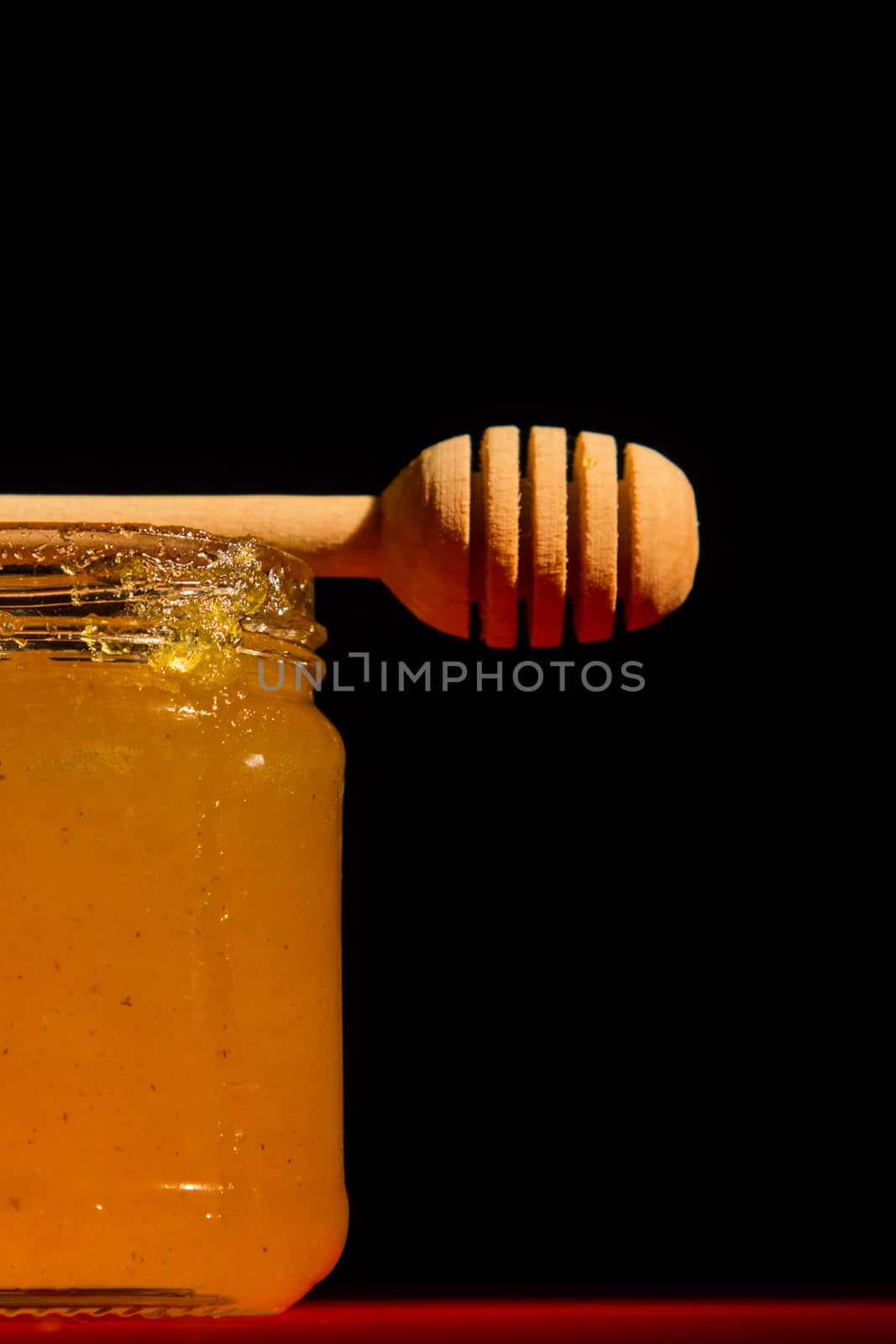 Honey with dipper on red wooden background with the the play of light and shadow